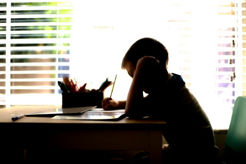 Young person at desk writing with a pencil