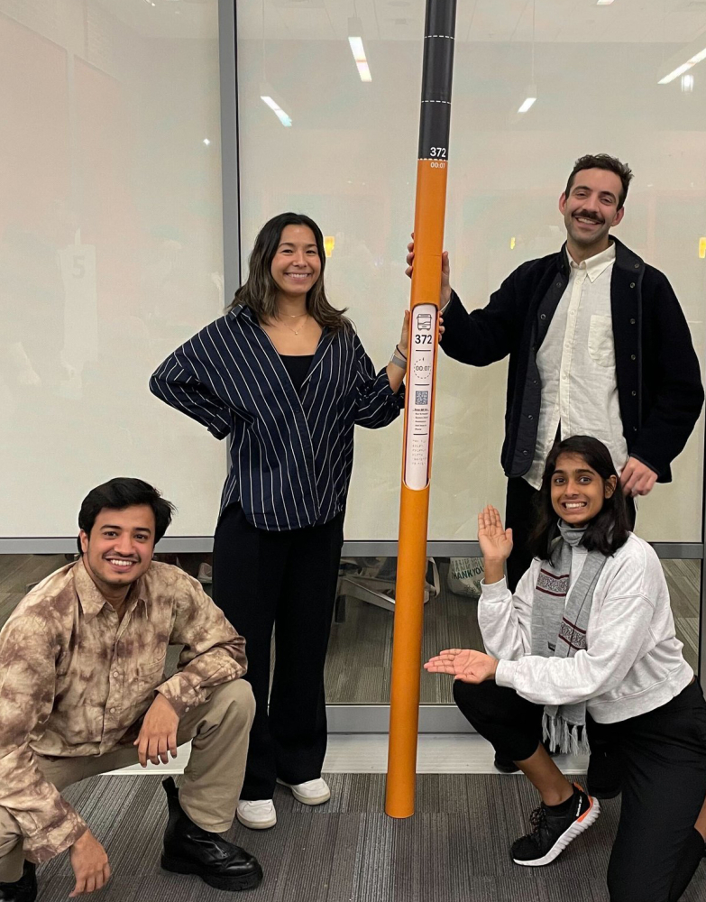 Team of four students posing with their physical prototype of the bus beacon pole, which stands several feet taller than the students.